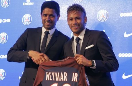 Brazilian soccer star Neymar holds his team shirt as he shakes with the chairman of Paris Saint-Germain Nasser Al-Khelaifi during a press conference in Paris Friday, Aug. 4, 2017. Neymar arrived in Paris on Friday the day after he became the most expensive player in soccer history when completing his blockbuster transfer to Paris Saint-Germain from Barcelona for 222 million euros ($262 million).(AP Photo/Michel Euler)
