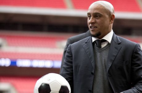 Former Brazil national soccer team player Roberto Carlos holds a ball as he attends a group photo session pitchside as a guest of FIFA Presidential Candidate Gianni Infantino after unveiling his 90 day plan that he will implement if he is elected FIFA President, at Wembley Stadium in London, Monday, Feb. 1, 2016. (AP Photo/Matt Dunham)