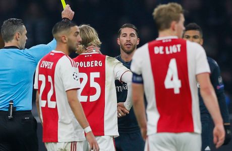 This Wednesday Feb. 13, 2019, image shows referee Damir Skomina, left, showing a yellow card to Real's Sergio Ramos, center, after a foul on Ajax's Kasper Dolberg during the first leg, round of sixteen, Champions League soccer match between Ajax and Real Madrid at the Johan Cruyff ArenA in Amsterdam, Netherlands. UEFA is investigating reported comments by Real Madrid captain Sergio Ramos that he intentionally got a yellow card to provoke a favorable Champions League ban. (AP Photo/Peter Dejong)