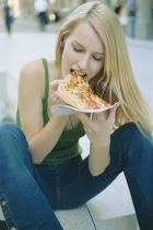 Young woman sitting in street eating slice of pizza, close-up