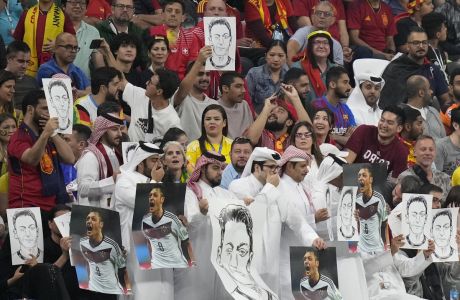 Spectators hold photos of Forman German international Mesut Ozil on the stands and cover their mouths during the World Cup group E soccer match between Spain and Germany, at the Al Bayt Stadium in Al Khor , Qatar, Sunday, Nov. 27, 2022. (AP Photo/Matthias Schrader)
