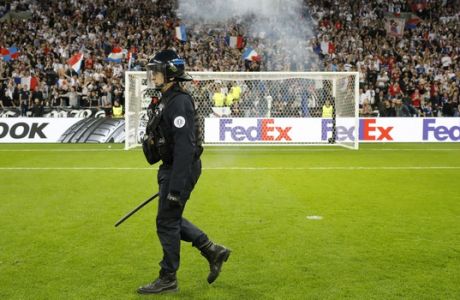 A police officer walks on the pitch as supporters invade it, a few minutes before the Europa League quarterfinal soccer match between Lyon and Besiktas, in Decines, near Lyon, central France, Thursday, April 13, 2017. (AP Photo/Laurent Cipriani)
