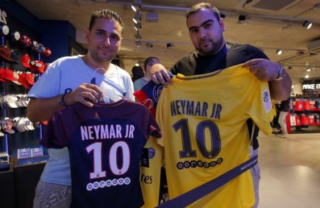 PSG supporters hold up soccer shirts bearing the name of Brazilian soccer star Neymar in the Paris Saint Germain store in Paris Friday, Aug. 4, 2017. Neymar was set to arrive in Paris on Friday the day after he became the most expensive player in soccer history when completing his blockbuster transfer to Paris Saint-Germain from Barcelona for 222 million euros ($262 million).(AP Photo/Michel Euler)
